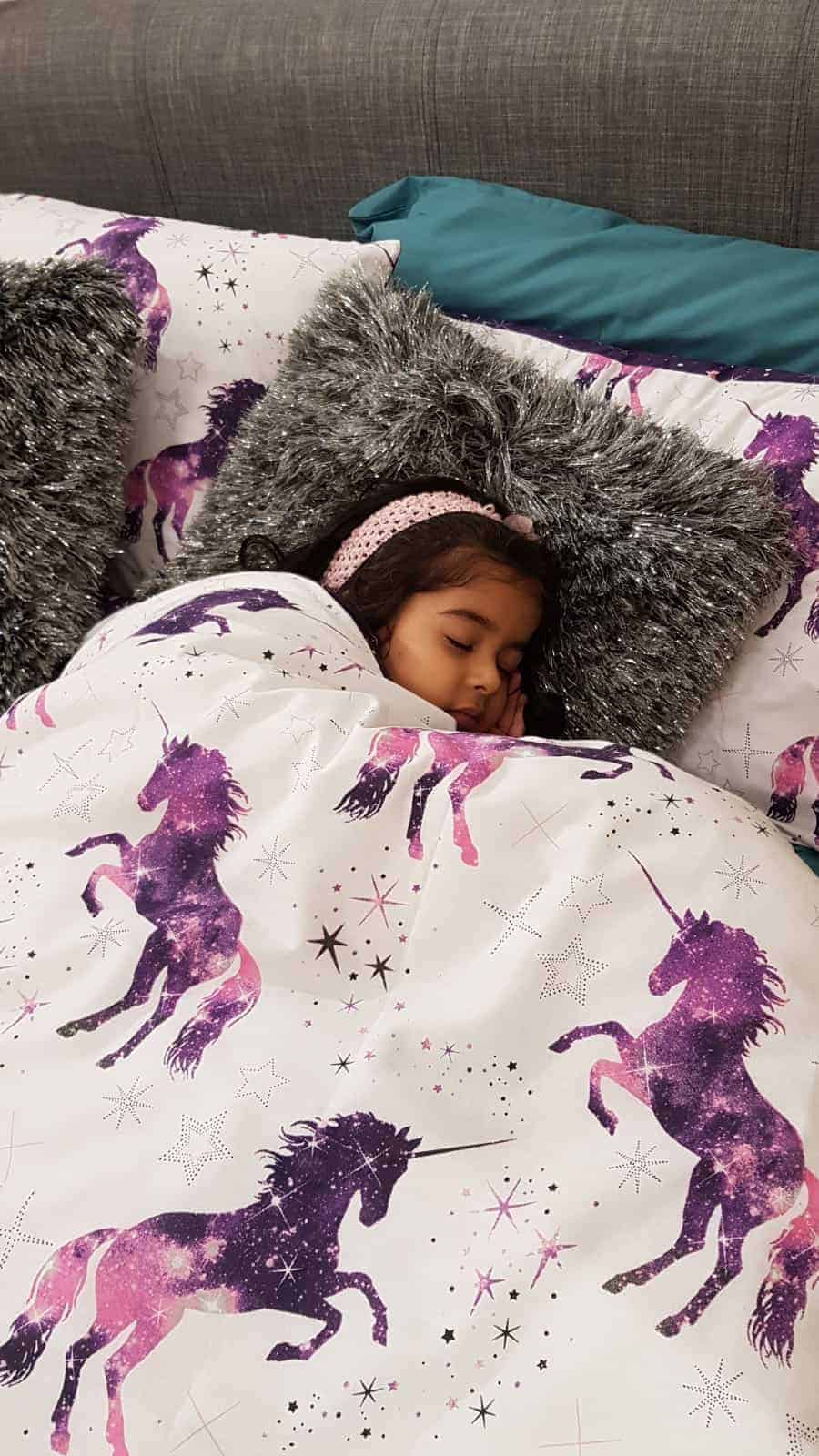 Young girl sleeping in a bed with purple unicorn duvet