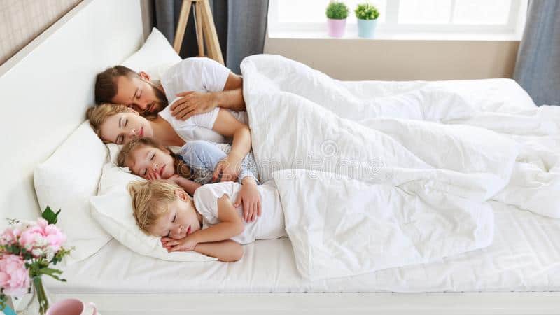 family asleep in bed with white sheets